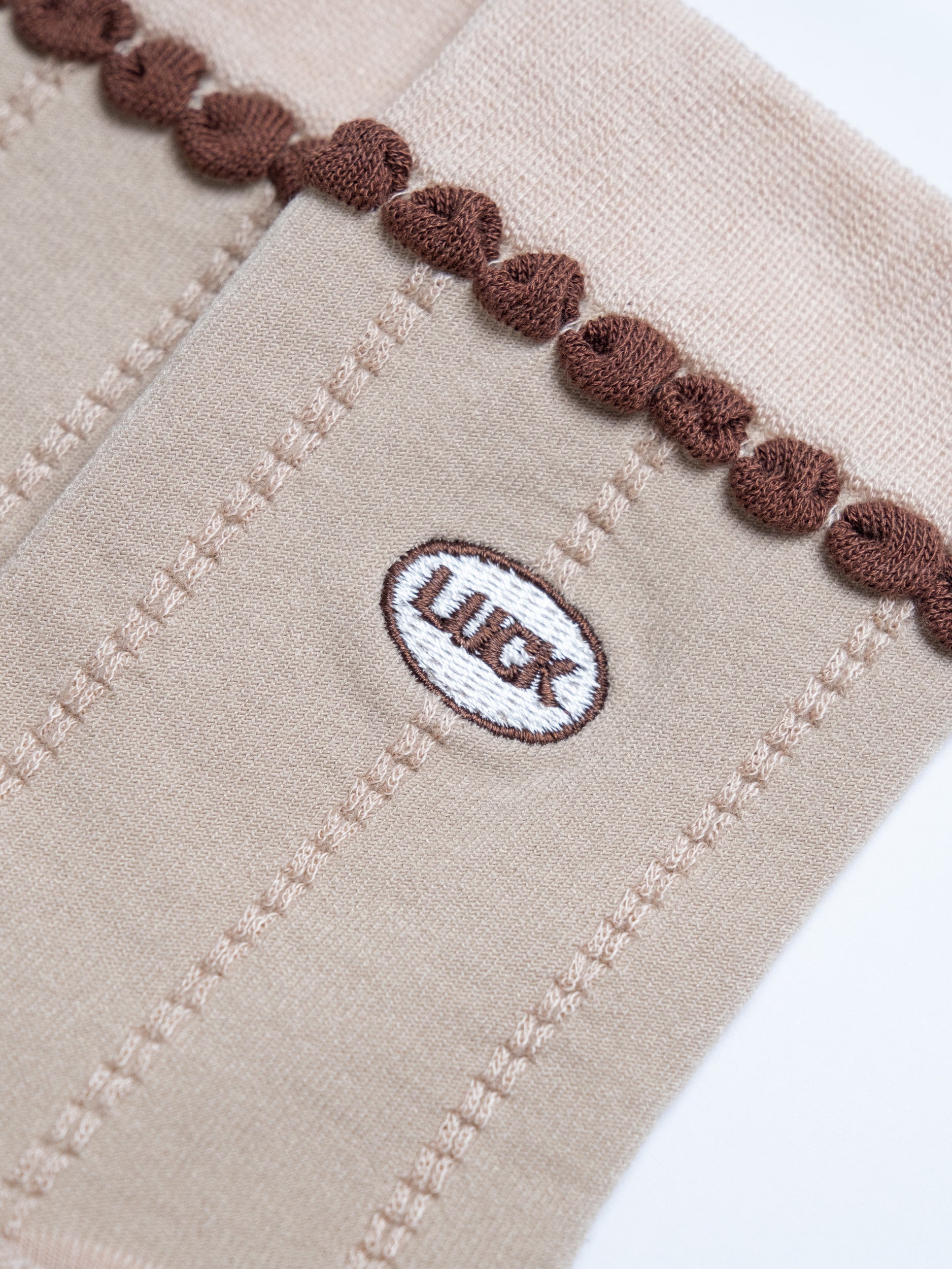 Close-up of beige fabric with brown trim and a logo on a white background