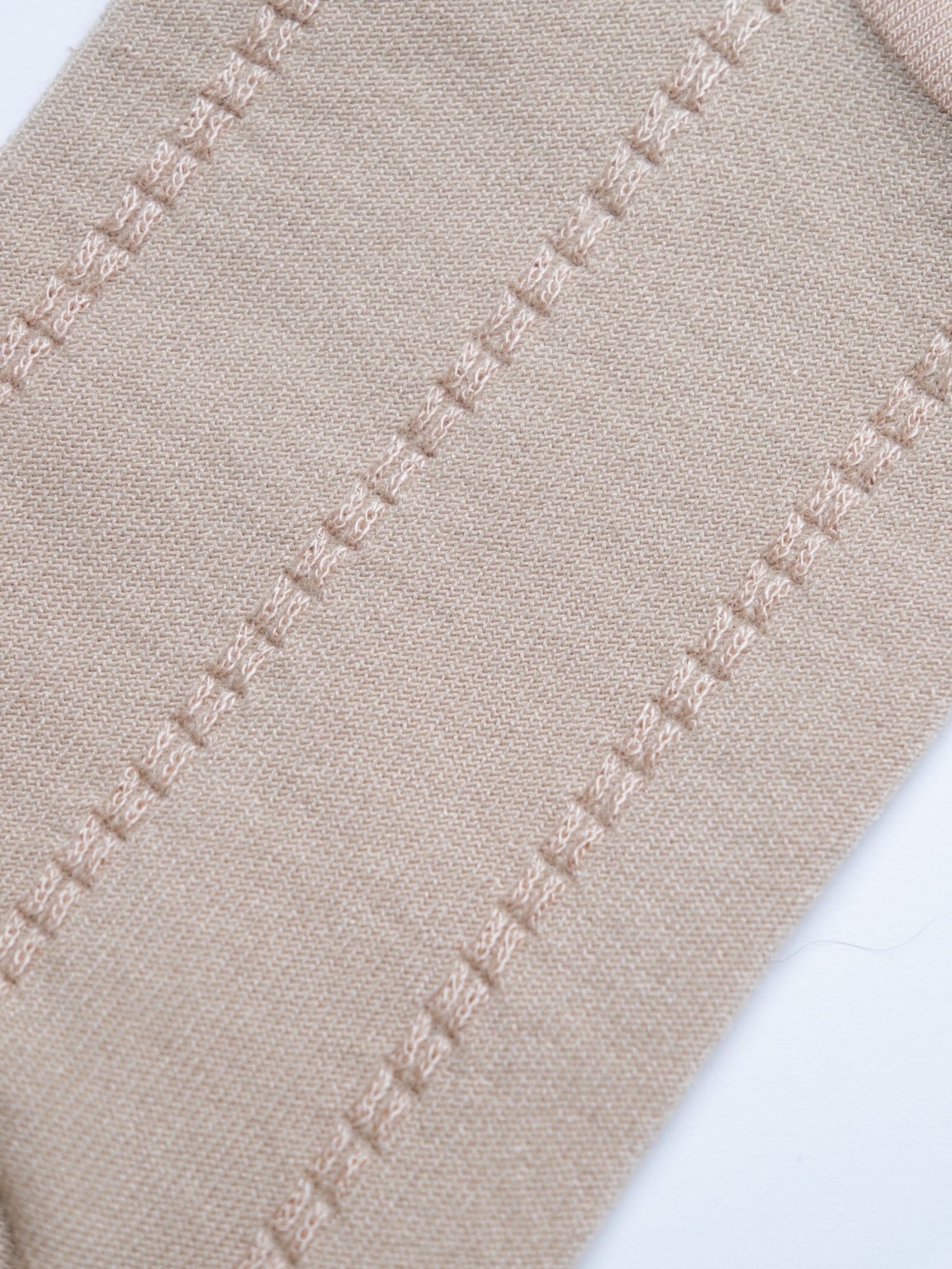 Close-up of beige fabric with a decorative stitch pattern on a white background