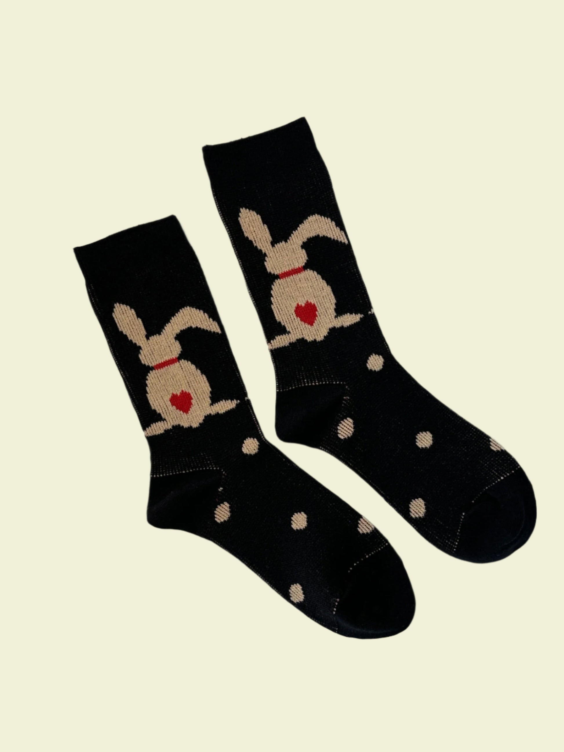Black socks with white polka dots and beige cat designs on a light gray background